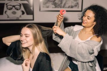 Two friends help each other install hair rollers.